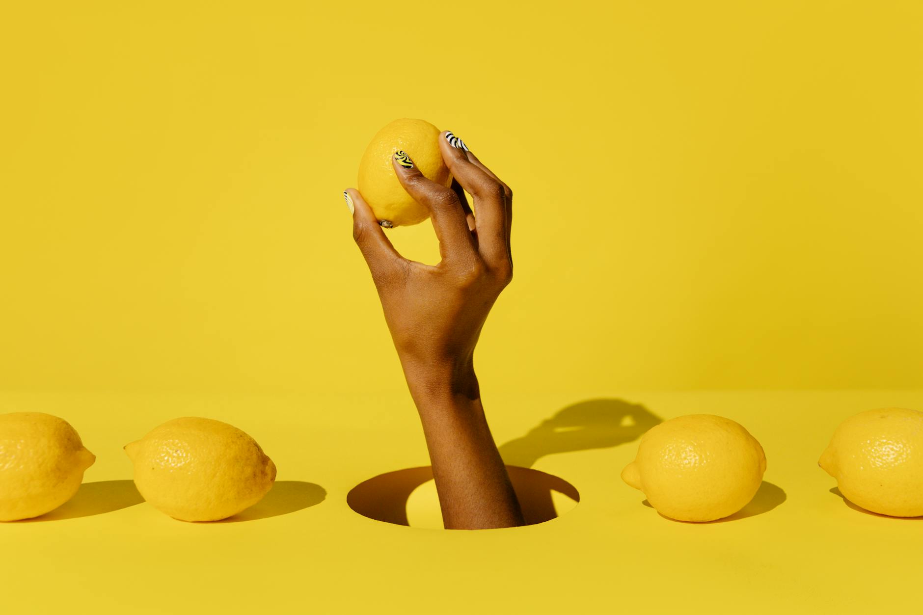 Hand holding a fresh lemon against a vibrant yellow background, symbolizing citrusy refreshment and sensory awakening