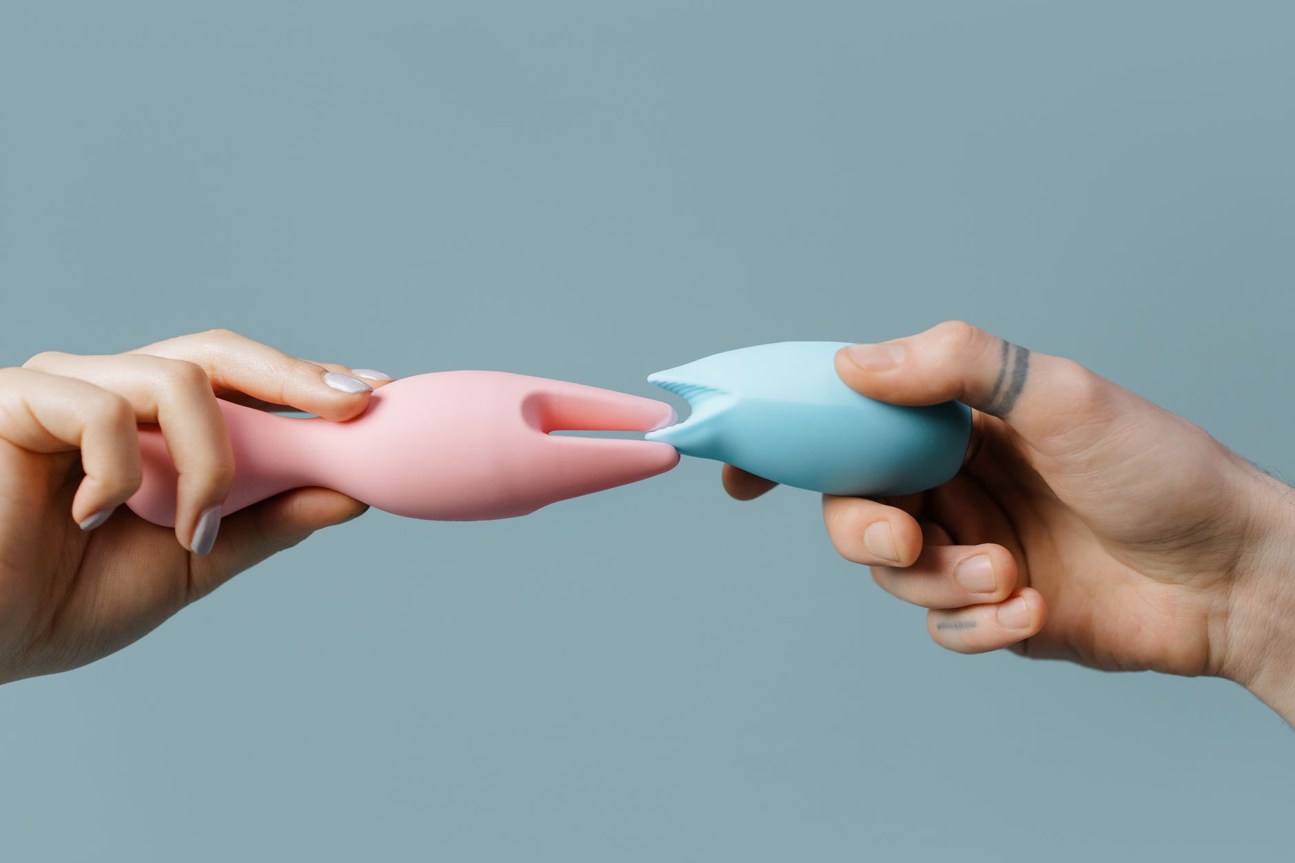 Hands holding pastel-colored silicone clitoral vibrators and adult toys.