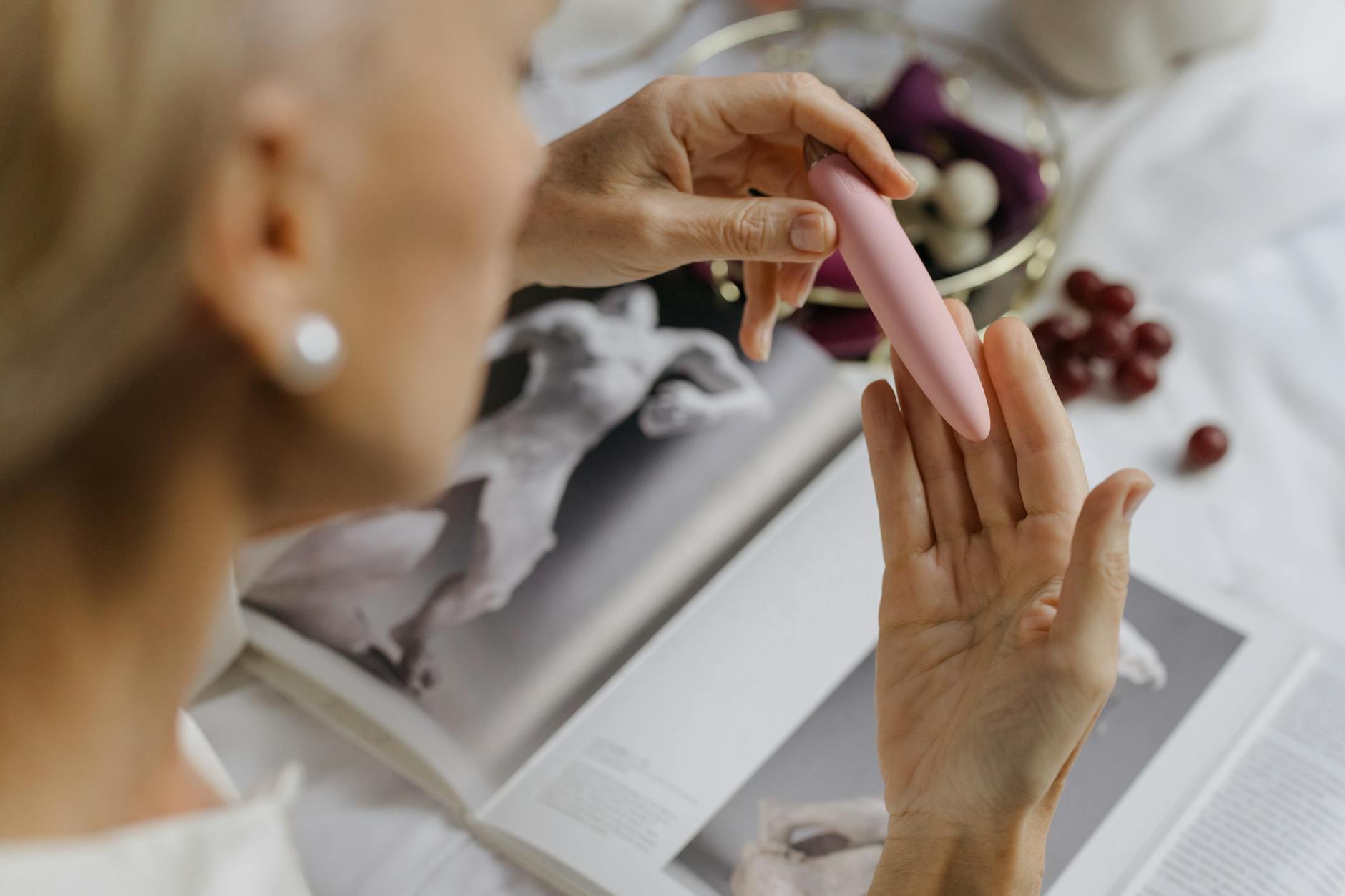 Close-up of hands holding a pink silicone vibrator with personal wellness items in soft focus