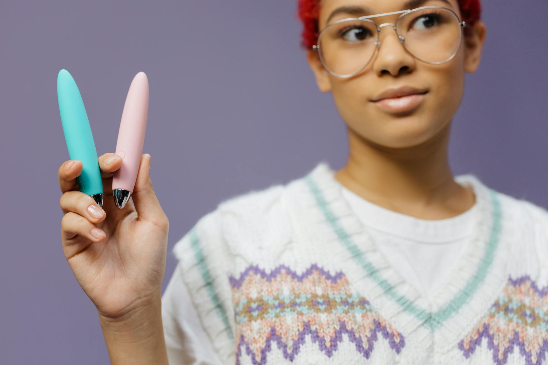 A woman holding colorful personal vibrators against a purple background, representing diverse pleasure tools