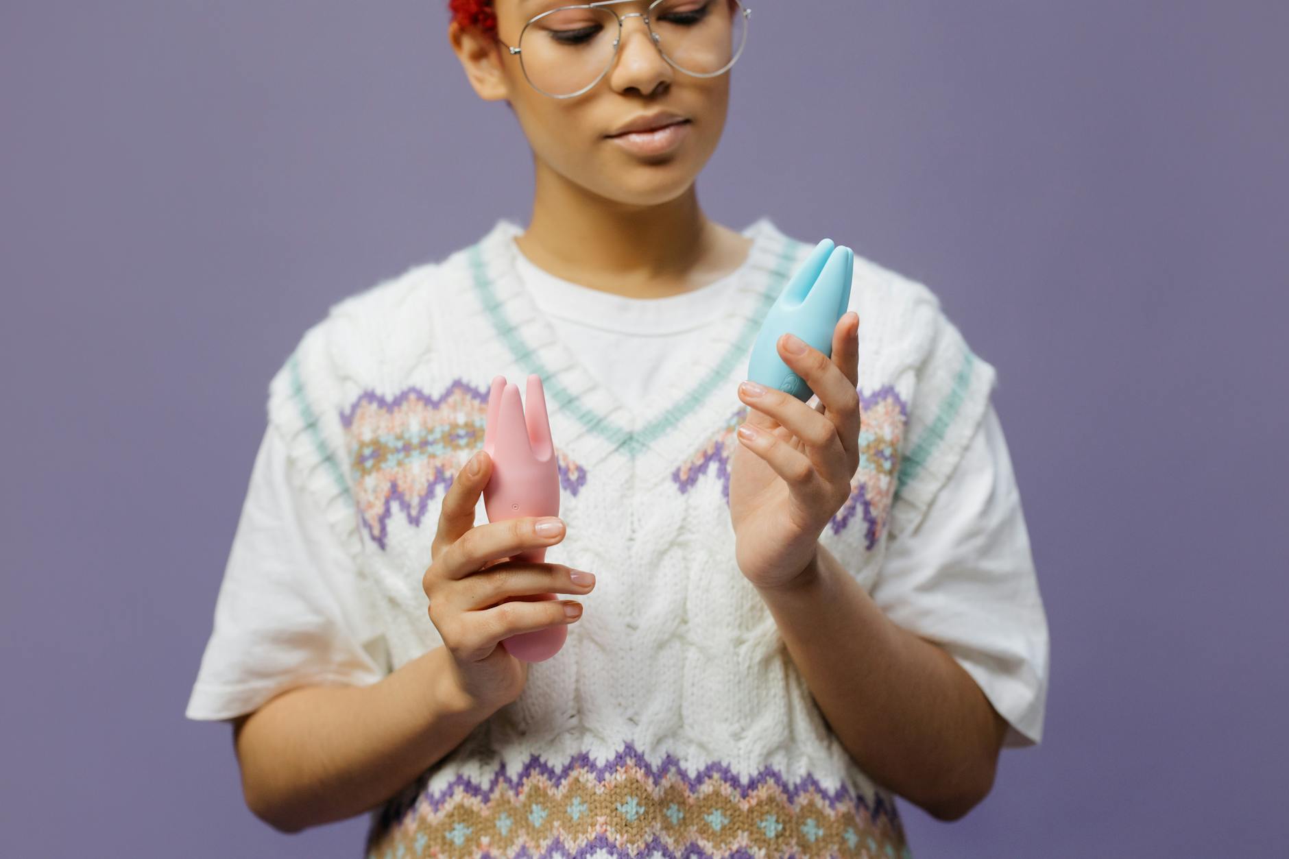 Woman holding blue and pink silicone clitoral vibrators, exploring sensation recovery options.