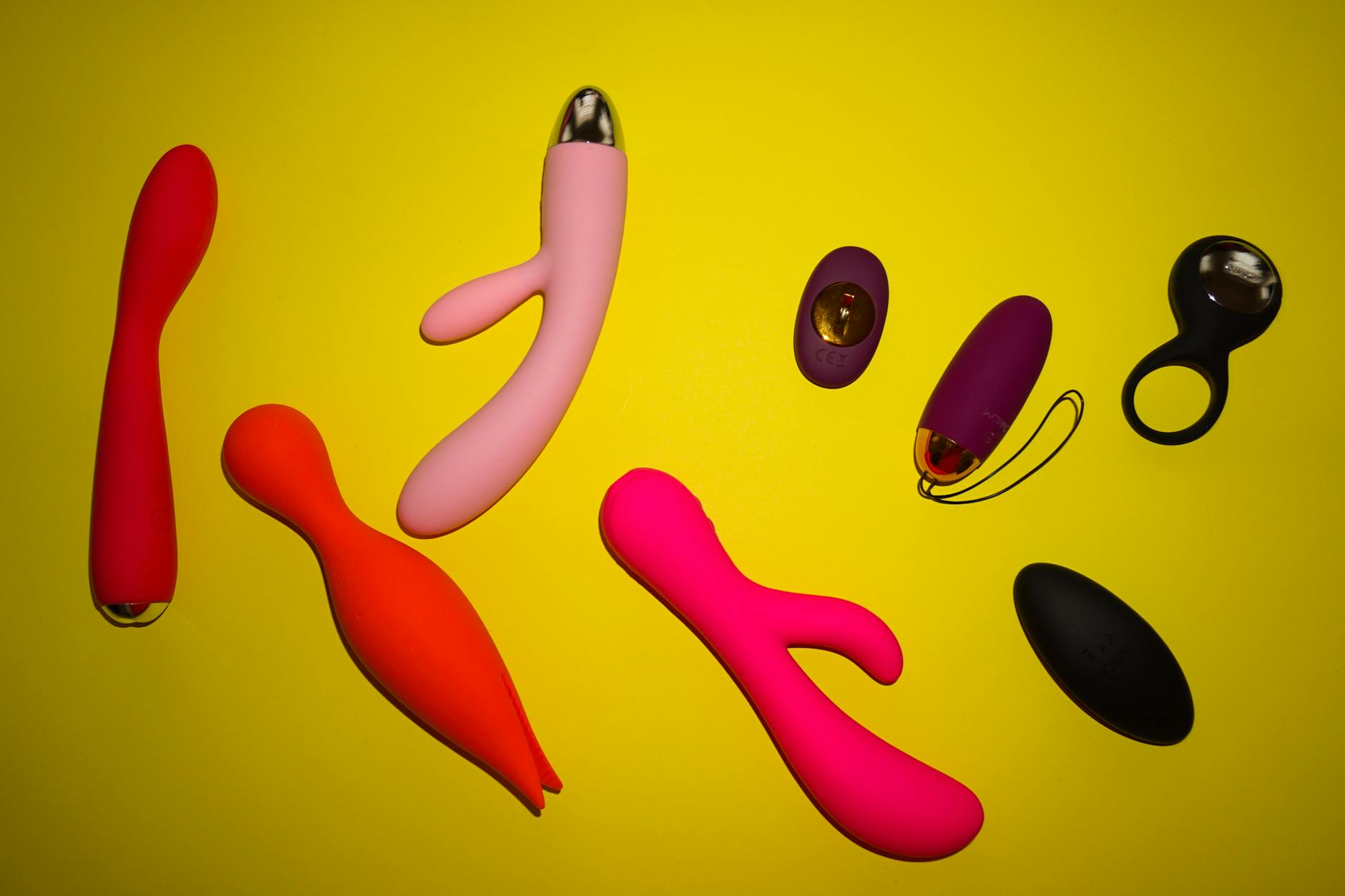 Colorful arrangement of sex toys on a bright yellow background showcasing different design shapes