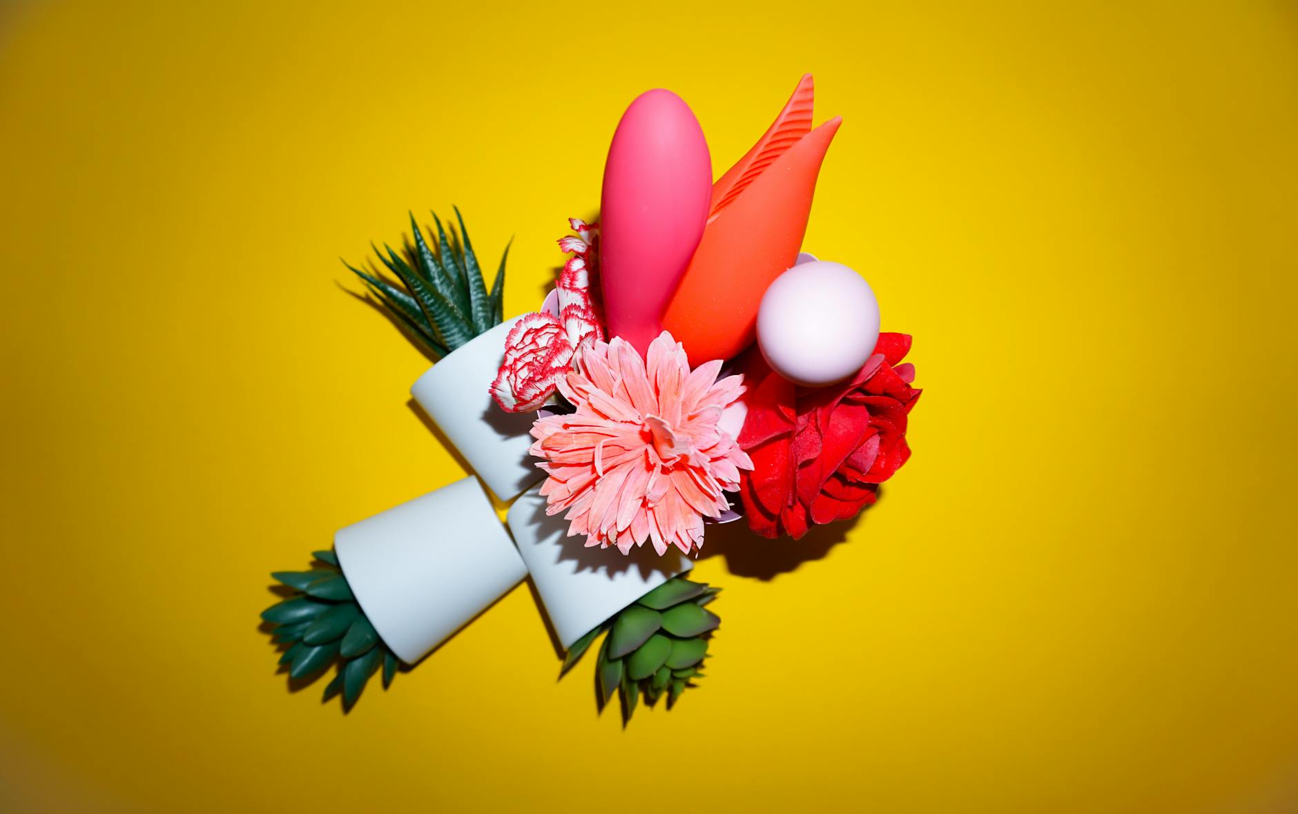 Blue vibrator surrounded by flowers and citrus on a bright yellow background