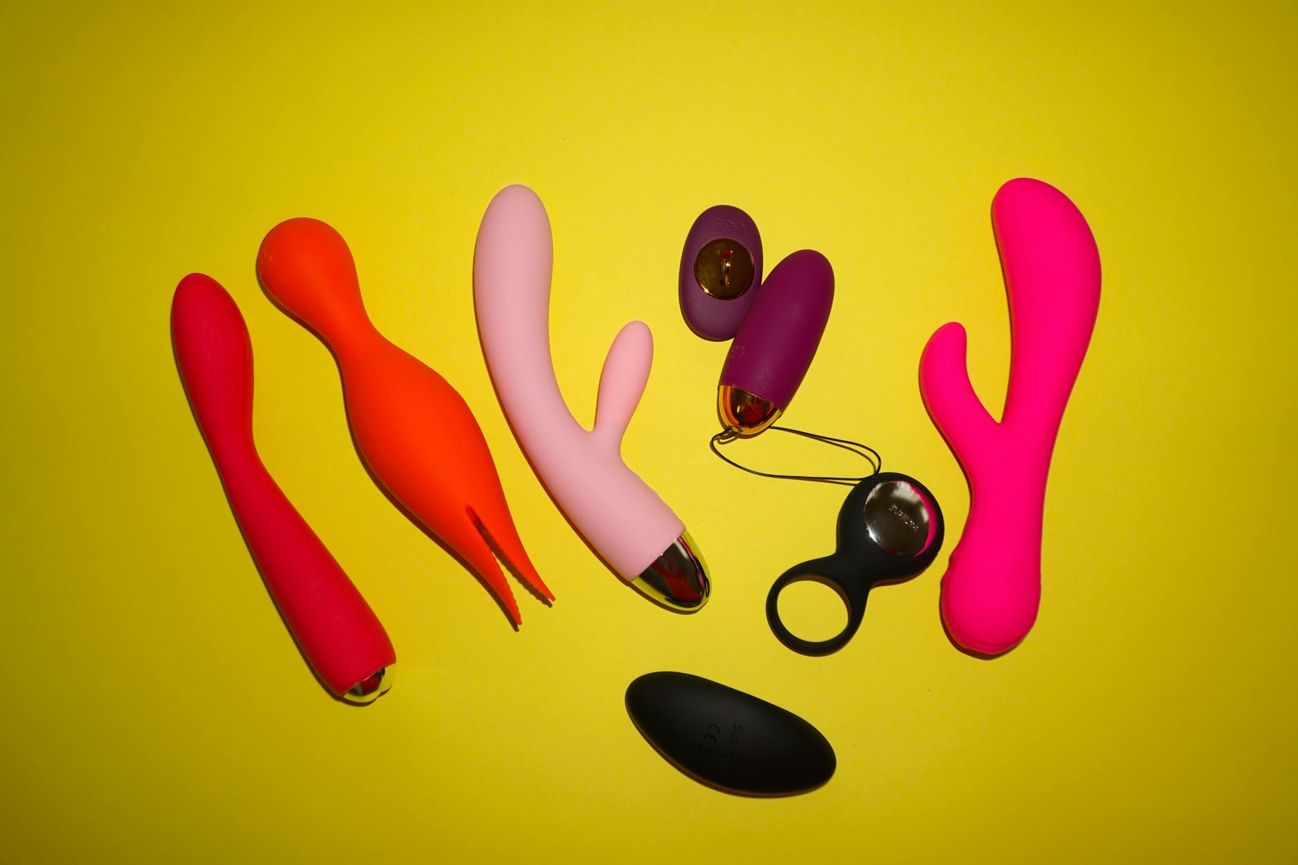 Colorful vibrators arranged on a bright yellow background, showcasing modern adult toy design and variety.