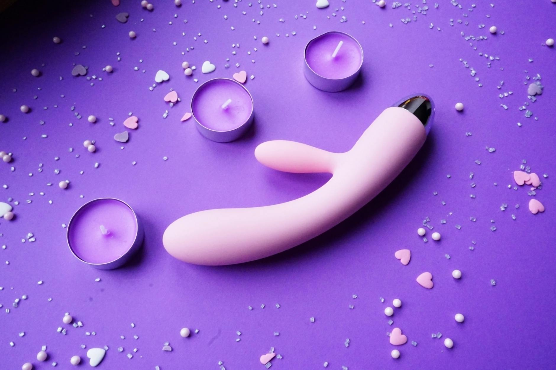 Vibrateur rose sur fond violet avec confettis cœurs et bougies pour une ambiance romantique
